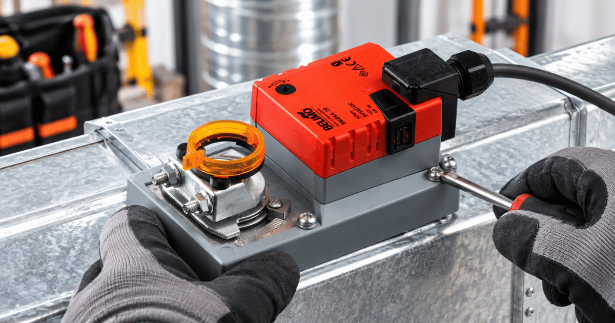 Engineer diagnosing a Belimo damper actuator fault on ductwork with manual override ring and screwdriver